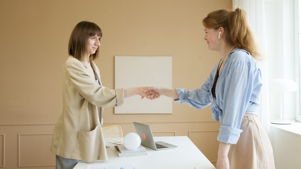Two women shaking hands, smiling with mutual respect