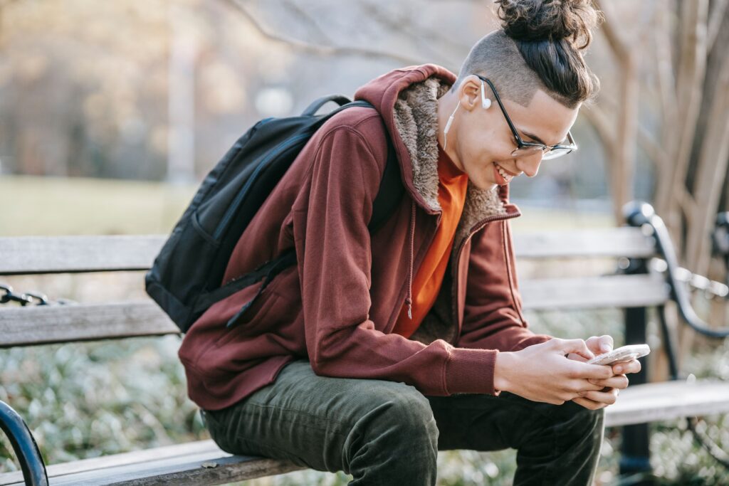 Young man smiling while casually texting on his phone, writing naturally like talking to a friend