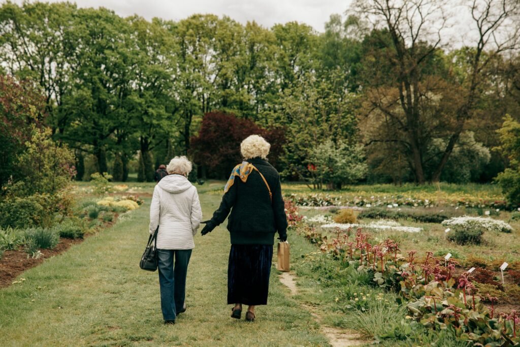 Two elderly women walking together in a garden, illustrating the daily movement and social connection linked to longevity