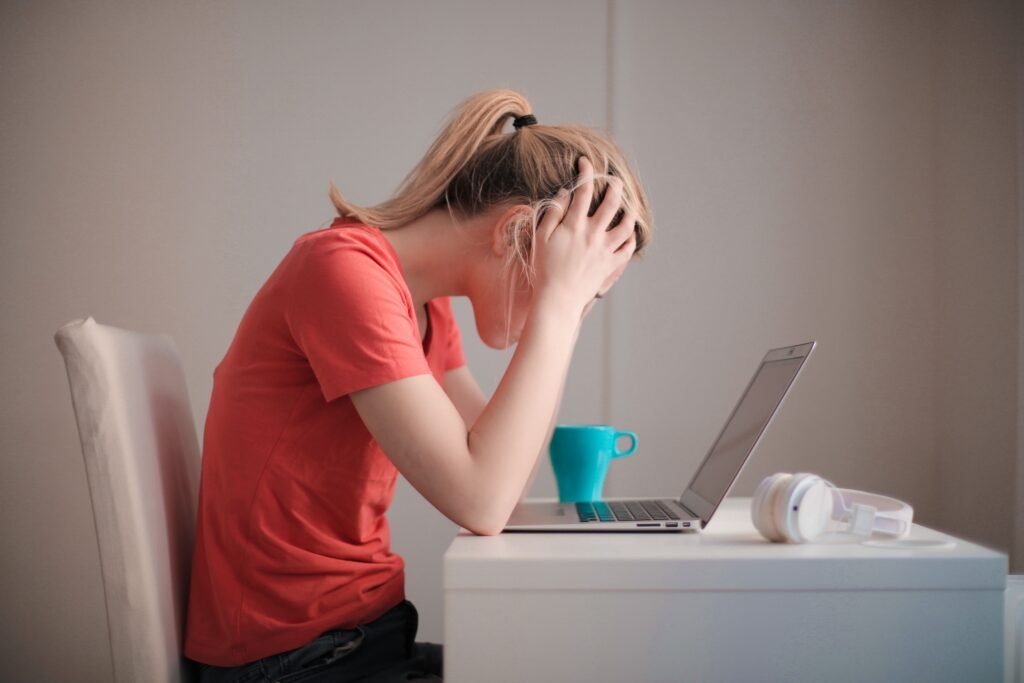 Stressed woman holding her head at a desk, illustrating common signs of a dysregulated nervous system
