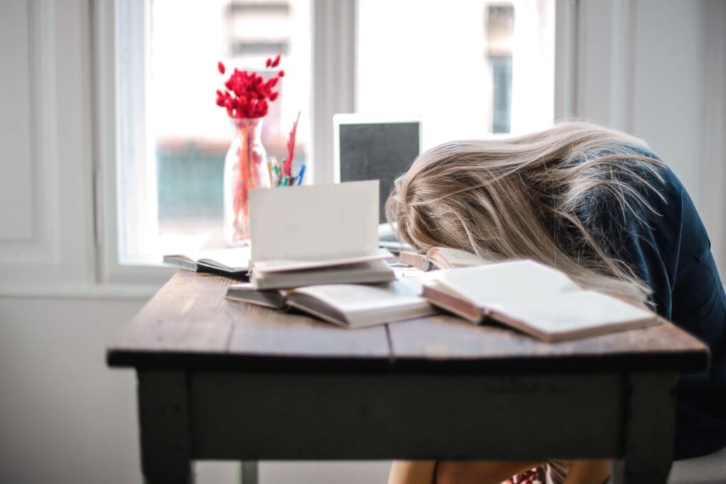 Exhausted person resting head on a pile of books, illustrating burnout from overly ambitious big goals
