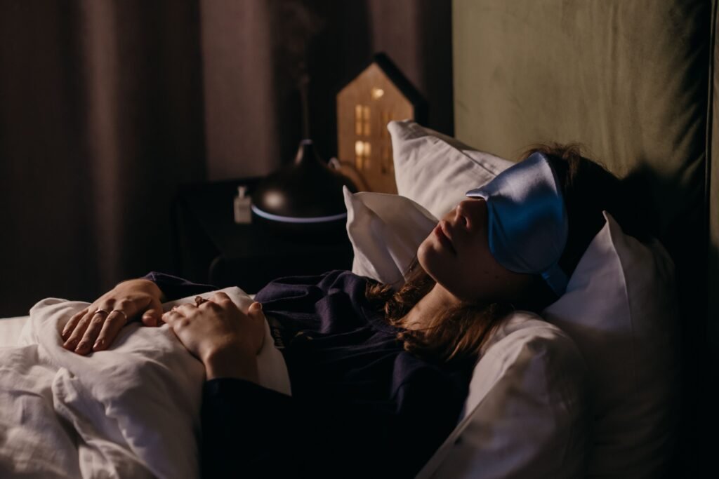 Woman sleeping with an eye mask in a dark, cozy bedroom, illustrating the importance of a dark sleep environment
