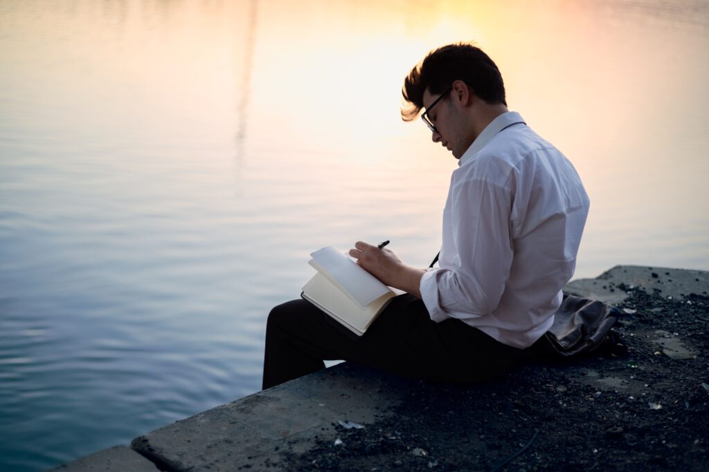 Man journaling by the water at sunset - daily reflection habit