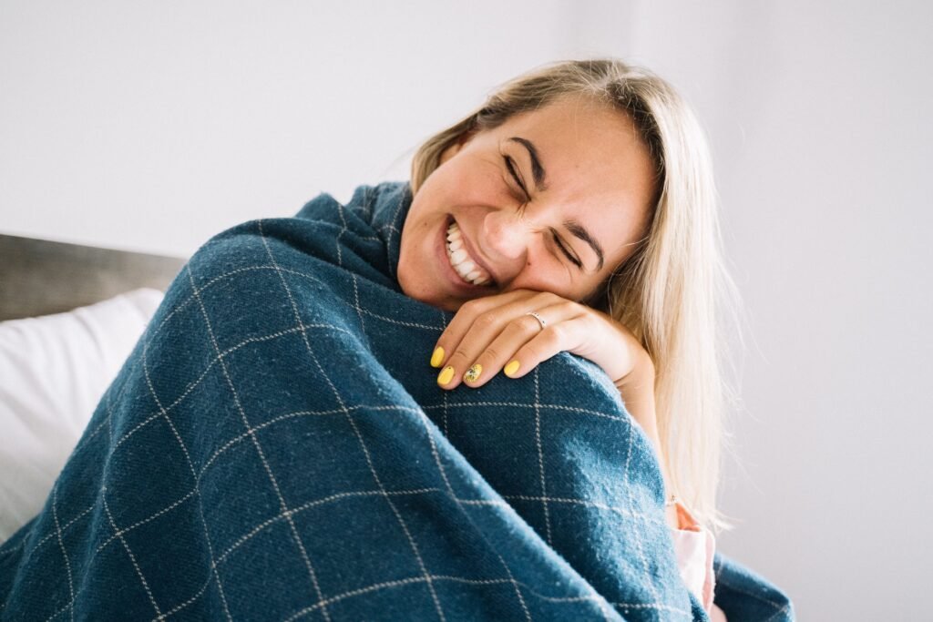 Woman laughing joyfully while wrapped in a blanket, representing the long-term emotional benefits of better sleep