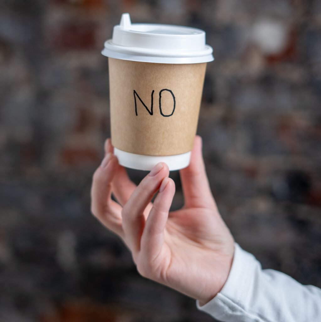 Hand holding a paper coffee cup with the word NO written on the sleeve, symbolizing the decision to quit coffee forever.
