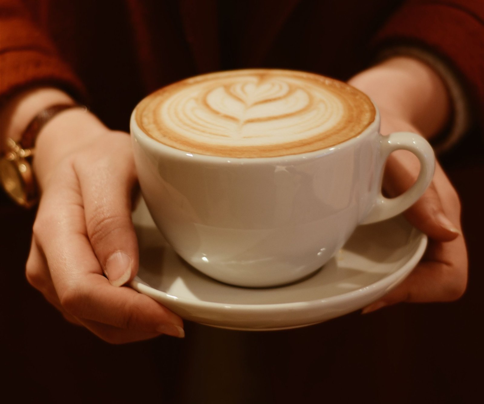 Person holding cappuccino coffee cup with latte art