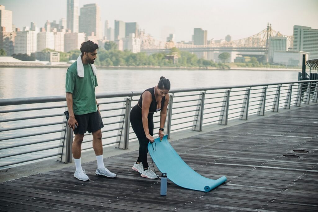 Man and woman preparing for an outdoor morning workout with a yoga mat by the riverside