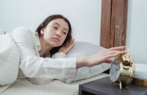 Tired woman lying in bed reaching out to turn off a gold alarm clock