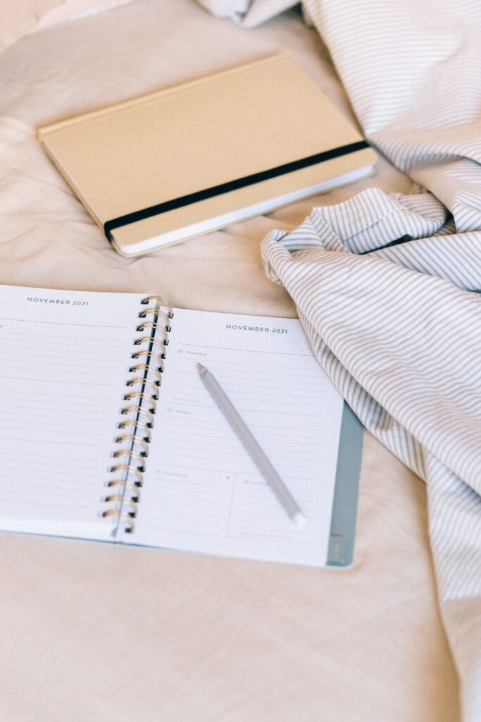 Open daily planner with a pen resting on the page, next to a notebook on a bed