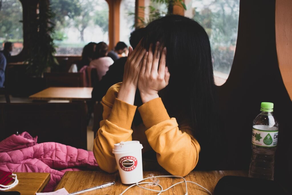 Frustrated person covering face with hands next to a coffee cup, illustrating caffeine withdrawal.